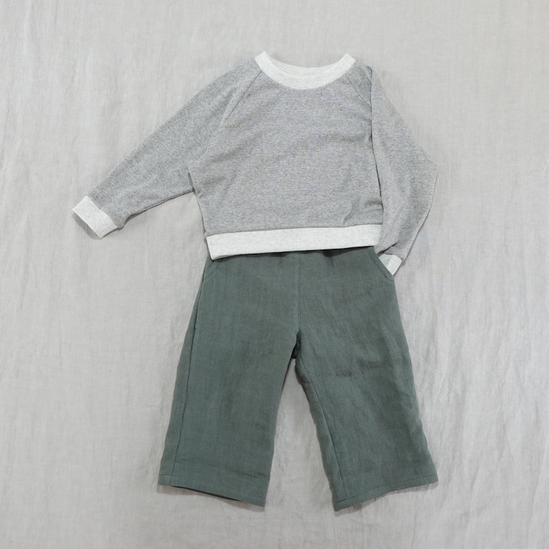Pode incluir: Uma camisa de manga comprida cinza e branca com uma cal&ccedil;a verde.