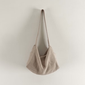 May include: A beige linen tote bag with a single strap hanging from a hook on a white wall.