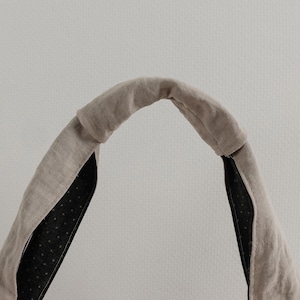 May include: A beige fabric headband with a knotted top detail. The exterior is a solid light brown linen-like material, while the interior lining is a dark charcoal fabric featuring a pattern of small, evenly spaced white polka dots.