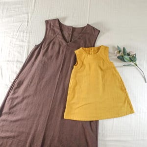 Könnte beinhalten: Zwei ärmellose Leinenkleider, eines braun und eines gelb. Das braune Kleid hat einen V-Ausschnitt und das gelbe Kleid einen runden Ausschnitt.
