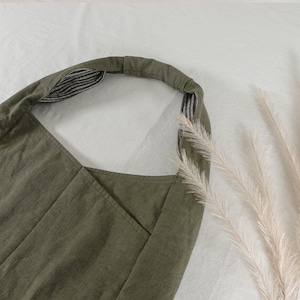 May include: An olive green hobo bag featuring a wide, integrated shoulder strap. The interior of the strap is lined with a black and white striped fabric. The exterior of the bag has a visible seam running vertically down the center of the front panel.