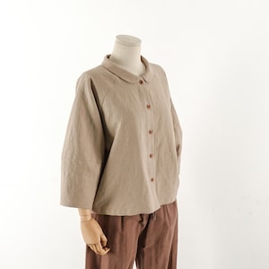 May include: A beige linen shirt with a peter pan collar and button closure. The shirt has a relaxed fit and three-quarter sleeves.