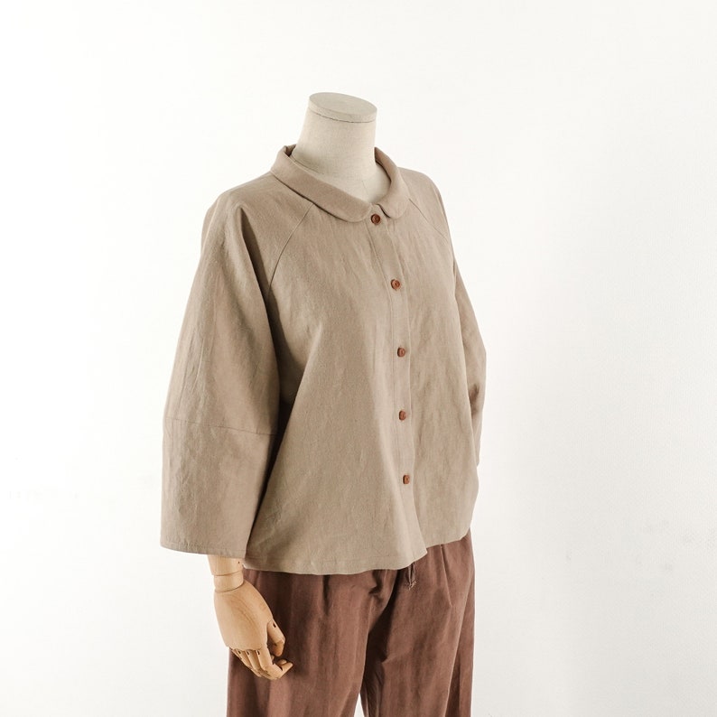 May include: A beige linen shirt with a peter pan collar and button closure. The shirt has a relaxed fit and three-quarter sleeves.
