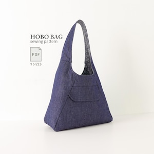 Pode incluir: Uma bolsa hobo de ganga azul escura com uma alça de ombro única e um bolso frontal. O texto HOBO BAG sewing pattern, PDF e 3 SIZES é visível. O forro interior apresenta um padrão floral cinzento escuro e branco visível na abertura.