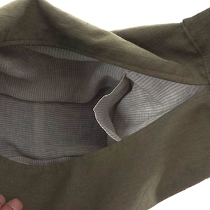 May include: An olive green bag with a textured exterior and a light gray interior lining featuring a subtle white pinstripe pattern. The bag includes an open internal pocket on the side, revealing the contrasting fabric construction of the interior.