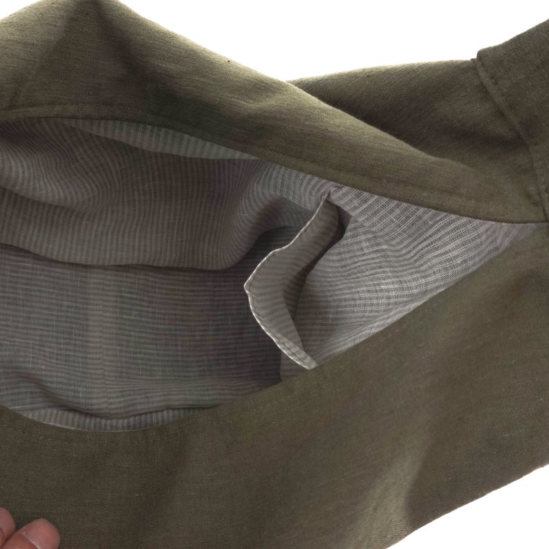 May include: An olive green bag with a textured exterior and a light gray interior lining featuring a subtle white pinstripe pattern. The bag includes an open internal pocket on the side, revealing the contrasting fabric construction of the interior.