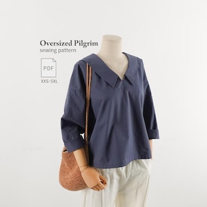 Könnte beinhalten: Ein marineblaues Langarmshirt mit weitem Kragen und V-Ausschnitt auf einer Schaufensterpuppe. Der Text "Oversized Pilgrim sewing pattern" und "PDF XXS-5XL" ist sichtbar. Eine braune geflochtene Tasche hängt über einer weißen Hose.