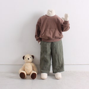 Pode incluir: Uma camisola castanha com um bolso canguru e mangas compridas. A camisola &eacute; combinada com cal&ccedil;as verde-oliva.