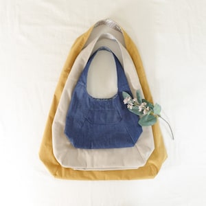 May include: Three fabric tote bags nested inside each other. The outer bag is mustard yellow, the middle bag is beige, and the inner bag is dark blue denim.