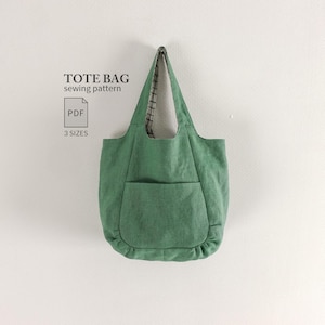 Pode incluir: Uma bolsa tote verde sálvia com um bolso frontal e detalhe franzido na base. O texto TOTE BAG sewing pattern PDF 3 SIZES é visível à esquerda. A bolsa possui duas alças de ombro e um forro interno com um padrão de grade escuro.