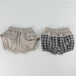May include: Two pairs of baby bloomers. One pair is beige with a ruffle trim. The other pair is black and white gingham.