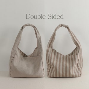 May include: Two hobo-style shoulder bags with the text Double Sided centered above them. One bag is solid beige, while the other features vertical beige and white stripes. Both bags have a single knotted handle and a visible exterior pocket.