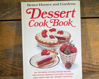 May include: A white cookbook with the title "Dessert Cook Book" in red and black lettering. The cover features a pie with whipped cream and strawberries, and a bowl of strawberries. The text below the title reads "246 Top-Rated Kitchen-Tested Recipes Spectacular Desserts for Every Occasion Make-Ahead and Diet Dessert Favorites."
