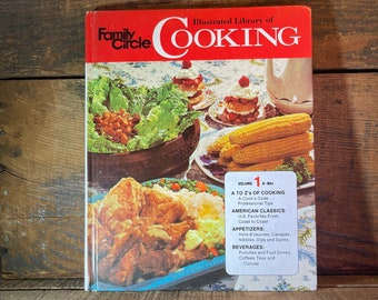 May include: A vintage cookbook titled "Family Circle Illustrated Library of Cooking" with a red cover and a volume number 1. The cover features a variety of food items, including a bowl of salad, corn on the cob, and a casserole dish.