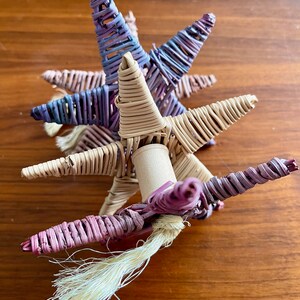 May include: A woven unicorn toy with a pink, purple, and beige color scheme. The unicorn has a long, flowing tail made of white yarn.