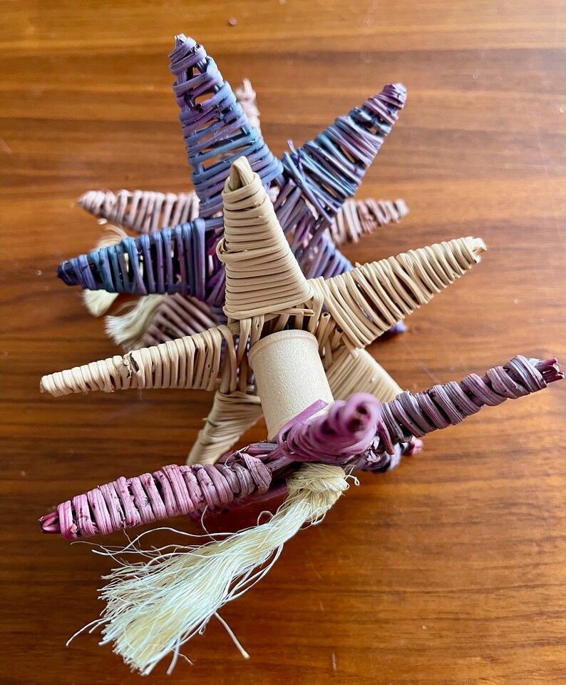 May include: A woven unicorn toy with a pink, purple, and beige color scheme. The unicorn has a long, flowing tail made of white yarn.