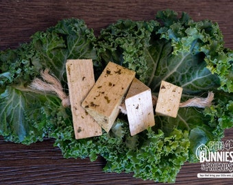 May include: Four wooden chew toys for rabbits, shaped like rectangles and triangles, with a natural brown color and green flecks. The toys are arranged on a bed of green kale leaves. The text "FUN 4 BUNNIES & FRIENDS" is visible in the lower right corner of the image.