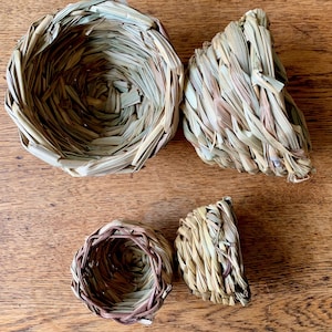 May include: Four woven straw bird nests of varying sizes. The nests are made of natural materials and have a rustic, earthy look.
