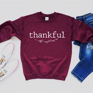 May include: A maroon sweatshirt with the word "thankful" printed in white with a small branch design underneath.