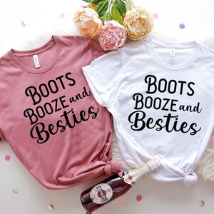 May include: Two t-shirts with the text "Boots Booze and Besties" printed on them. One shirt is pink and the other is white.