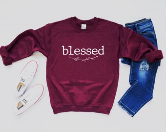 May include: Burgundy sweatshirt with the word "blessed" in white lettering with a small white floral design underneath.