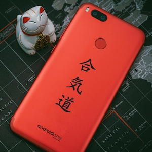 Puede incluir: Un teléfono inteligente rojo con el texto "androidone" y los caracteres japoneses "合気道" impresos en la parte posterior.