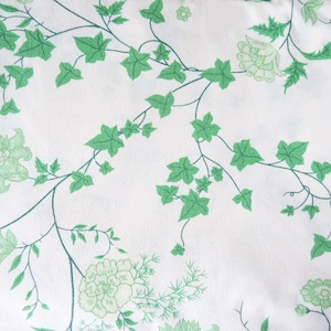 May include: White fabric with a green floral pattern. The pattern features leaves and flowers in a repeating design.