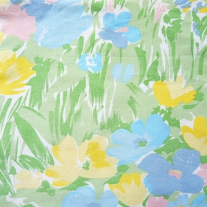 May include: A white fabric with a floral pattern featuring yellow, blue, and pink flowers on a green background.