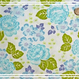 Könnte beinhalten: Weißer Stoff mit einem blauen und grünen Blumenmuster. Der Stoff zeigt ein sich wiederholendes Muster aus blauen Rosen und grünen Blättern auf weißem Hintergrund.