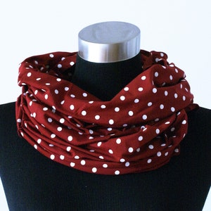Könnte beinhalten: Burgunderfarbener Loop-Schal mit weißem Polka-Dot-Muster. Der Schal ist um eine schwarze Schaufensterpuppe drapiert, was sein kreisförmiges Design zeigt. Der Stoff wirkt weich und leicht, geeignet für verschiedene Jahreszeiten.