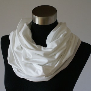 Könnte beinhalten: Ein weißer Infinity-Schal aus weichem Stoff, drapiert um eine schwarze Schaufensterpuppe.