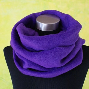 Könnte beinhalten: Ein violetter Fleece-Halswärmer oder -Schal. Der Halswärmer ist gefaltet und auf einer schwarzen Puppe ausgestellt.