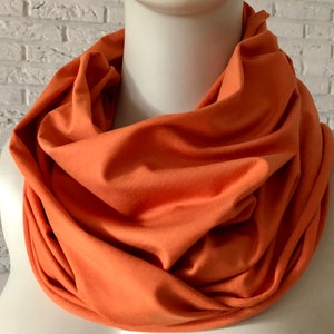 Könnte beinhalten: Ein weicher, orangefarbener Infinity-Schal aus dehnbarem Stoff. Der Schal ist gefaltet und um den Hals einer Schaufensterpuppe gelegt.