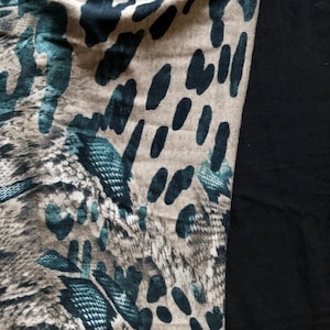 Könnte beinhalten: Ein Textil mit einem Muster aus dunkelblauen und schwarzen Punkten und einem schlangenlederartigen Design auf beigem Hintergrund. Die rechte Seite des Bildes ist einfarbig schwarz.