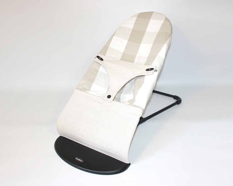 Puede incluir: Un asiento mecedor para beb&eacute;s a rayas beige y blancas con una base negra. El asiento tiene un asiento acolchado y un arn&eacute;s.