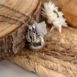 May include: Silver necklace with a silver charm of a baby's foot and a silver bell. The necklace has a gray tassel attached to it.
