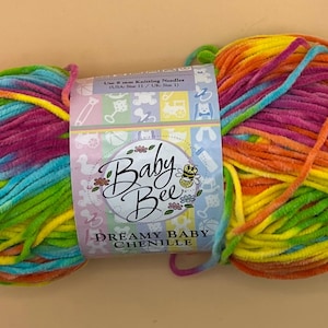 May include: A colorful skein of Baby Bee Dreamy Baby Chenille yarn. The yarn is a blend of vibrant colors including blue, green, yellow, orange, and pink. The label reads "Baby Bee Dreamy Baby Chenille".