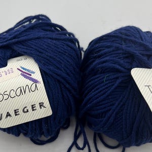 Könnte beinhalten: Zwei Knäuel dunkelblaues Garn mit weißen Etiketten, auf denen "Toscana" und "Jaeger" steht. Die Etiketten enthalten auch den Text "50 g" und "554.95".