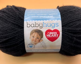 Può includere: Un gomitolo di filato nero con un'etichetta di carta che riporta il testo babyhugs e Red Heart. L'etichetta mostra la fotografia di un bambino, il testo 100% acrylic, no dye lot e light. Il filato è di colore nero solido con aspetto ritorto.