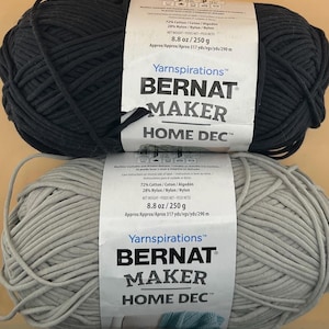 May include: Two balls of Bernat Maker Home Dec yarn, one dark grey and one light grey. Each ball weighs 250 g and is made of 72% cotton and 28% nylon. The labels include the text "Bernat Maker Home Dec".