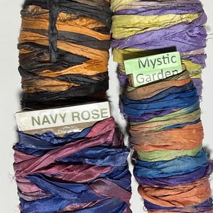 K&ouml;nnte beinhalten: Vier Spulen aus zerknittertem Seidenband, die um Pappkarten gewickelt sind. Die Spulen sind beschriftet mit Golden Harvest in Orange und Schwarz, Crocus in Gelb und Lila, Navy Rose in Marineblau und Pink sowie Mystic Garden in Blau, Orange und Gr&uuml;n.