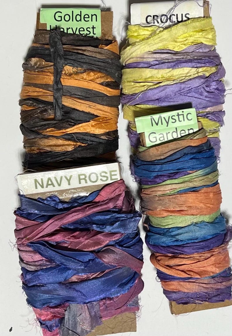 K&ouml;nnte beinhalten: Vier Spulen aus zerknittertem Seidenband, die um Pappkarten gewickelt sind. Die Spulen sind beschriftet mit Golden Harvest in Orange und Schwarz, Crocus in Gelb und Lila, Navy Rose in Marineblau und Pink sowie Mystic Garden in Blau, Orange und Gr&uuml;n.