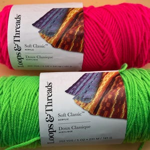 May include: Two skeins of Loops & Threads Soft Classic acrylic yarn, one hot pink and one bright green. Each skein is labelled with the brand name, yarn type, and yardage information. Suitable for knitting and crochet projects.