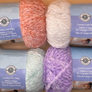 May include: A collection of colorful yarn skeins in shades of peach, white, mint green, and lavender. Each skein has a label that reads "Country Loom Baby". Ideal for knitting and crochet projects.