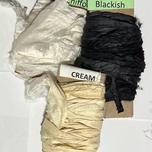 K&ouml;nnte beinhalten: Drei Bandspulen auf Pappkarten gewickelt. Eine Spule ist mit White Chiffon und wei&szlig;em Stoff, eine mit Blackish und schwarzem Stoff und eine mit CREAM und cremefarbenem Stoff beschriftet. Die B&auml;nder haben eine zerknitterte Textur.