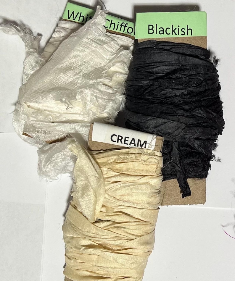 K&ouml;nnte beinhalten: Drei Bandspulen auf Pappkarten gewickelt. Eine Spule ist mit White Chiffon und wei&szlig;em Stoff, eine mit Blackish und schwarzem Stoff und eine mit CREAM und cremefarbenem Stoff beschriftet. Die B&auml;nder haben eine zerknitterte Textur.