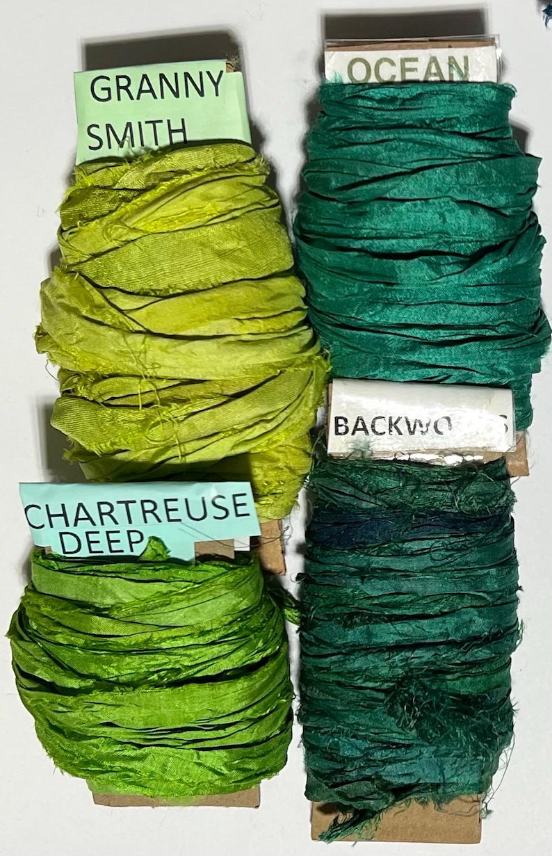 K&ouml;nnte beinhalten: Vier Seidenbandspulen in verschiedenen Gr&uuml;nt&ouml;nen. Die Etiketten tragen die Aufschriften Granny Smith, Ocean, Chartreuse Deep und Backwoods. Jede Spule besteht aus strukturiertem, zerknittertem Stoff, der um einen Pappkern gewickelt ist.