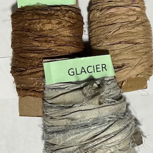 K&ouml;nnte beinhalten: Drei Spulen mit zerknittertem Band, die um Pappkerne gewickelt sind. Die obere linke Spule ist mit CARMEL beschriftet und dunkelbraun. Die obere rechte Spule ist mit SAND beschriftet und hellbeige. Die untere Spule ist mit GLACIER beschriftet und hellgrau.