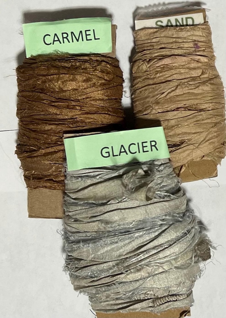 K&ouml;nnte beinhalten: Drei Spulen mit zerknittertem Band, die um Pappkerne gewickelt sind. Die obere linke Spule ist mit CARMEL beschriftet und dunkelbraun. Die obere rechte Spule ist mit SAND beschriftet und hellbeige. Die untere Spule ist mit GLACIER beschriftet und hellgrau.