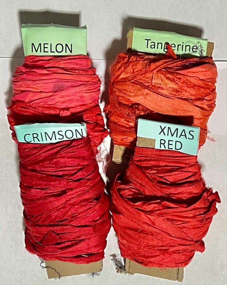 K&ouml;nnte beinhalten: Vier Spulen mit zerknittertem Band in den Farben Melon, Tangerine, Crimson und Xmas Red. Jede Spule hat ein hellgr&uuml;nes Papieretikett mit dem entsprechenden Farbnamen in schwarzer Schrift und ist mit strukturiertem, stoffartigem Band umwickelt.